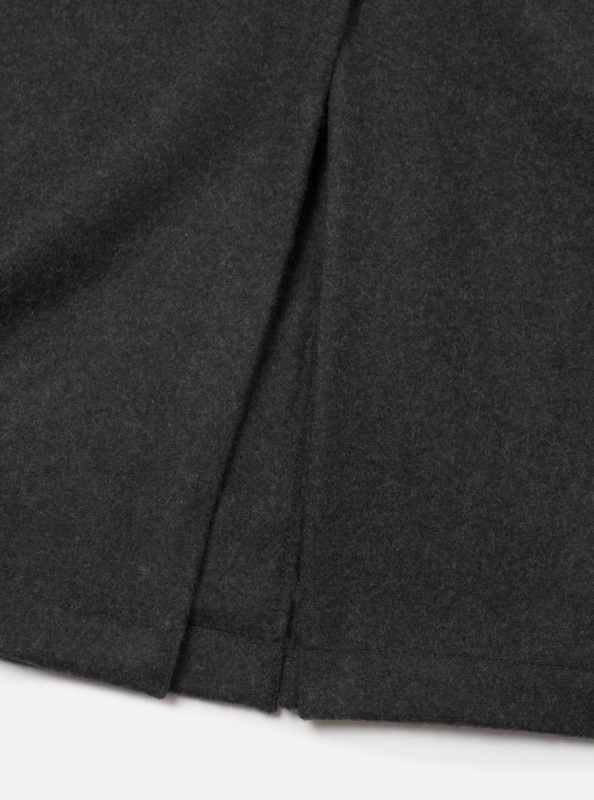 Close-up of the back hem and centre vent of a grey marl wool mac coat, laid flat on a white surface. The mélange fabric has a soft, lightly textured finish. The vent opening and neat hem are clearly visible, showing clean topstitching and precise construction.