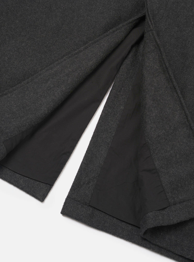 Close-up flat lay of the grey marl Mowbray Mac Coat hem and vent detail on a white surface. The back vent is open, revealing a black lining. The outer fabric is a medium-weight felted wool in dark charcoal marl. Topstitched edges finish the hem and vent cleanly.