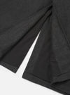 Close-up flat lay of the grey marl Mowbray Mac Coat hem and vent detail on a white surface. The back vent is open, revealing a black lining. The outer fabric is a medium-weight felted wool in dark charcoal marl. Topstitched edges finish the hem and vent cleanly.
