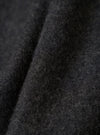 Close-up detail shot of the grey marl fabric on the Mowbray Mac Coat. The brushed wool textile shows a dense, fluffy surface with fine curled fibres and a dark charcoal tone with lighter grey flecks throughout. Soft folds reveal the fabric's weight and texture against a dark background.