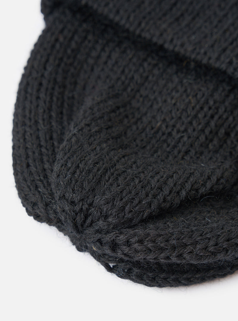 A close-up detail shot of the Black British Wool Short Watch Cap on a plain studio backdrop, highlighting the texture of the 100% British wool 5-gauge single rib knit and turn-up brim.