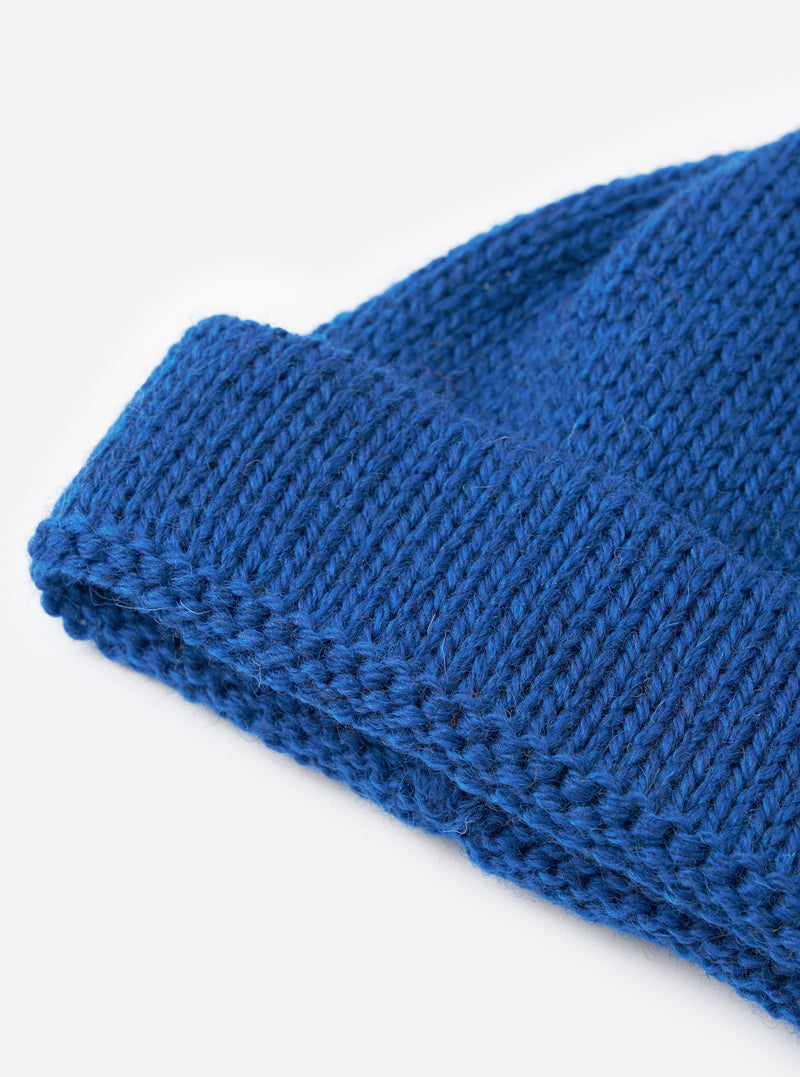An angled shot of the Bright Navy British Wool Short Watch Cap set against a neutral studio backdrop, highlighting its rolled edge cuff, short watch-cap style, and single rib knit pattern.