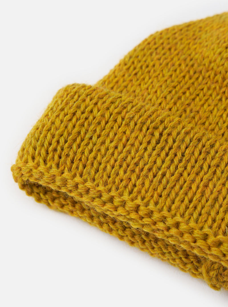 An angled view of the Mustard British Wool Short Watch Cap on a neutral plain background, showcasing its vibrant yellow tone, compact dock cap profile, and folded rib-knit cuff structure.