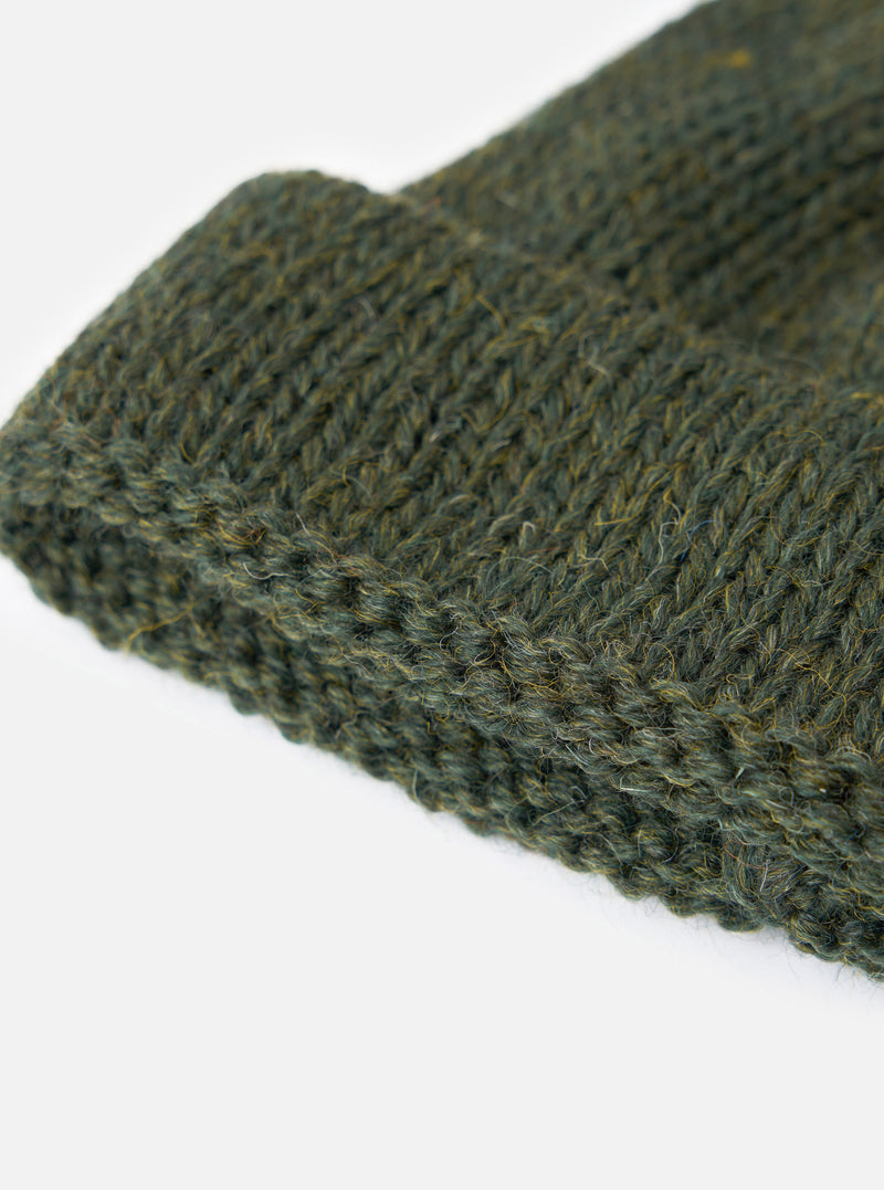 An angled view of the Olive British Wool Short Watch Cap set against a neutral studio backdrop, showing the compact watch cap silhouette, turned-up hem, and single rib knit pattern.