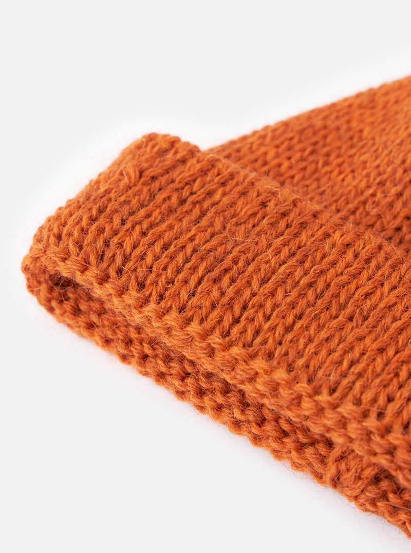 An alternate view of the Orange British Wool Short Watch Cap on a plain off-white background. The short knitted watch cap highlights its rich textured wool knit construction and turned-up brim.