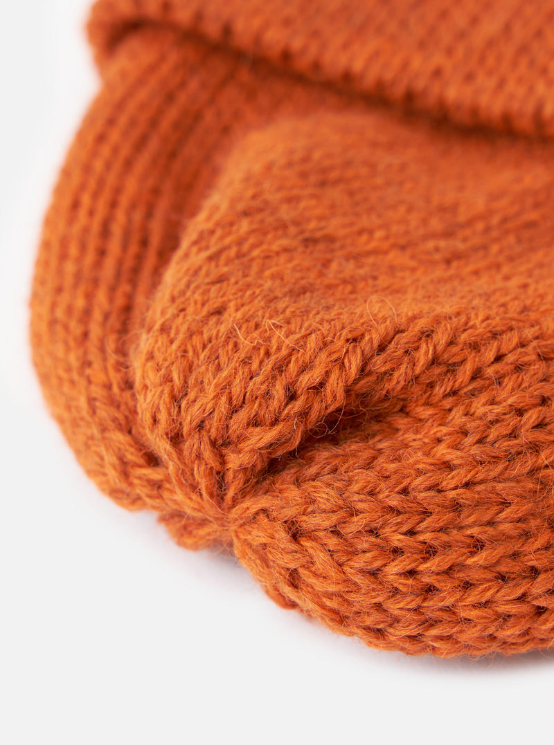 A detailed close-up shot of the Orange British Wool Short Watch Cap set against a neutral studio backdrop, highlighting the fine ribbing and bright orange British wool yarn detail.