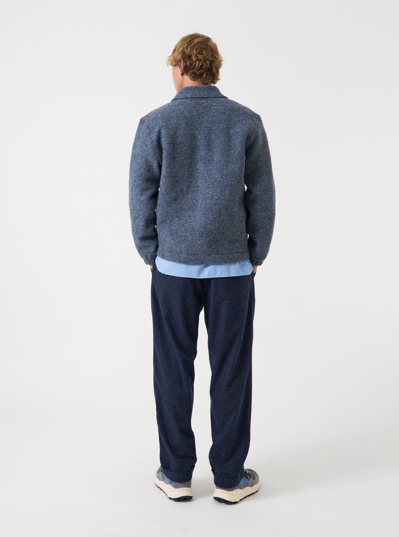 A male model wears the Slate Blue Wool Fleece Rams Jacket posed turned away from the camera against a neutral studio backdrop, highlighting the broad back fit, low shoulder seam, and relaxed drape.
