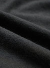 Close-up detail shot of the black recycled wool mix fabric, showing a soft, lightly brushed texture with fine fibres visible on the surface. The material has a dense, matte finish with gentle folds catching the light to reveal subtle tonal variation across the dark charcoal-black cloth.