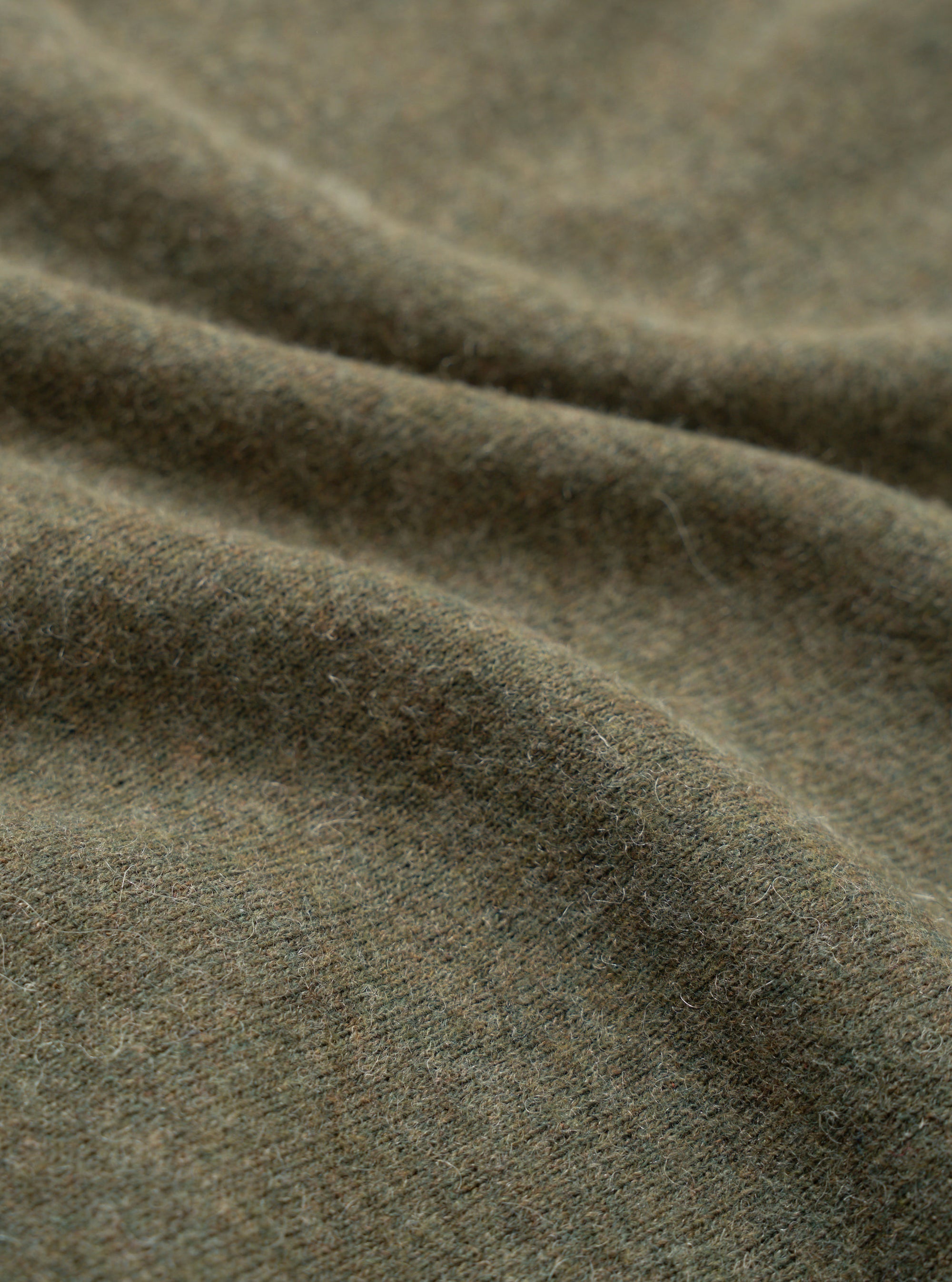 Close-up detail shot of the olive recycled wool mix fabric used in the pocket tee. The mélange knit shows a soft, brushed surface with fine fibres visible across its texture. Gentle folds in the fabric highlight its weight and drape.