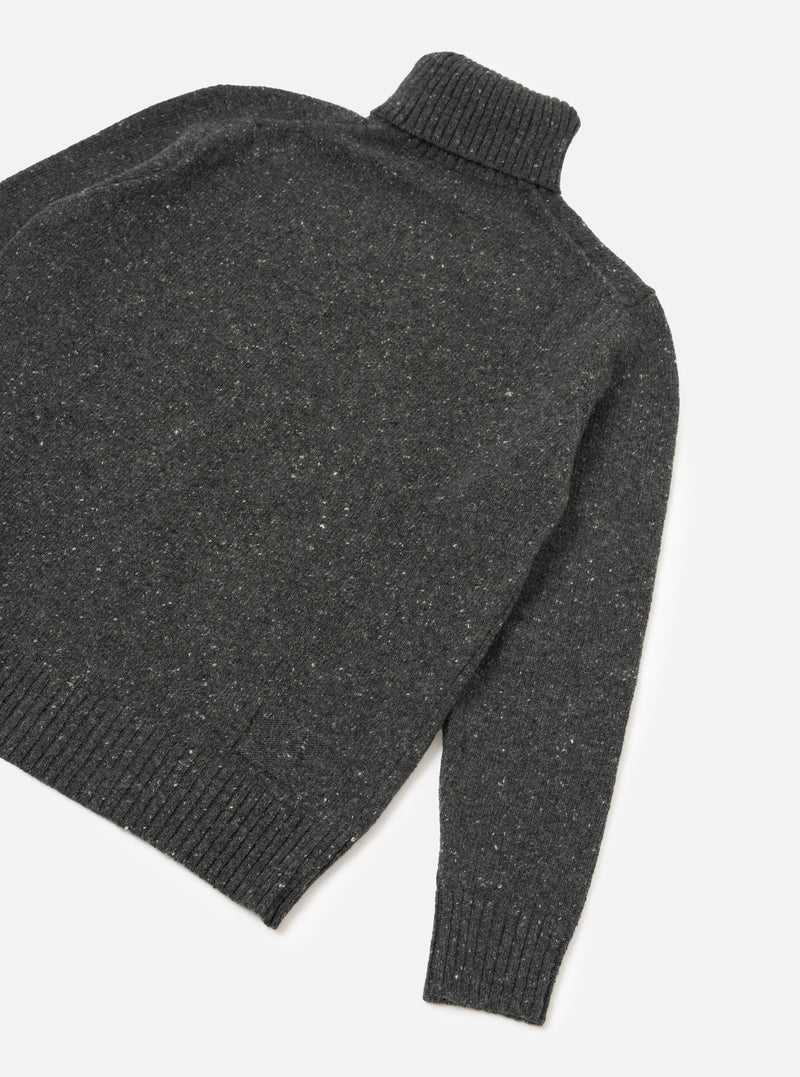 A side view of a model wearing the Black Wool Fleck Roll Neck on a plain background, highlighting the relaxed fit, ribbed cuffs, and soft recycled wool texture with subtle contrasting flecked detailing.