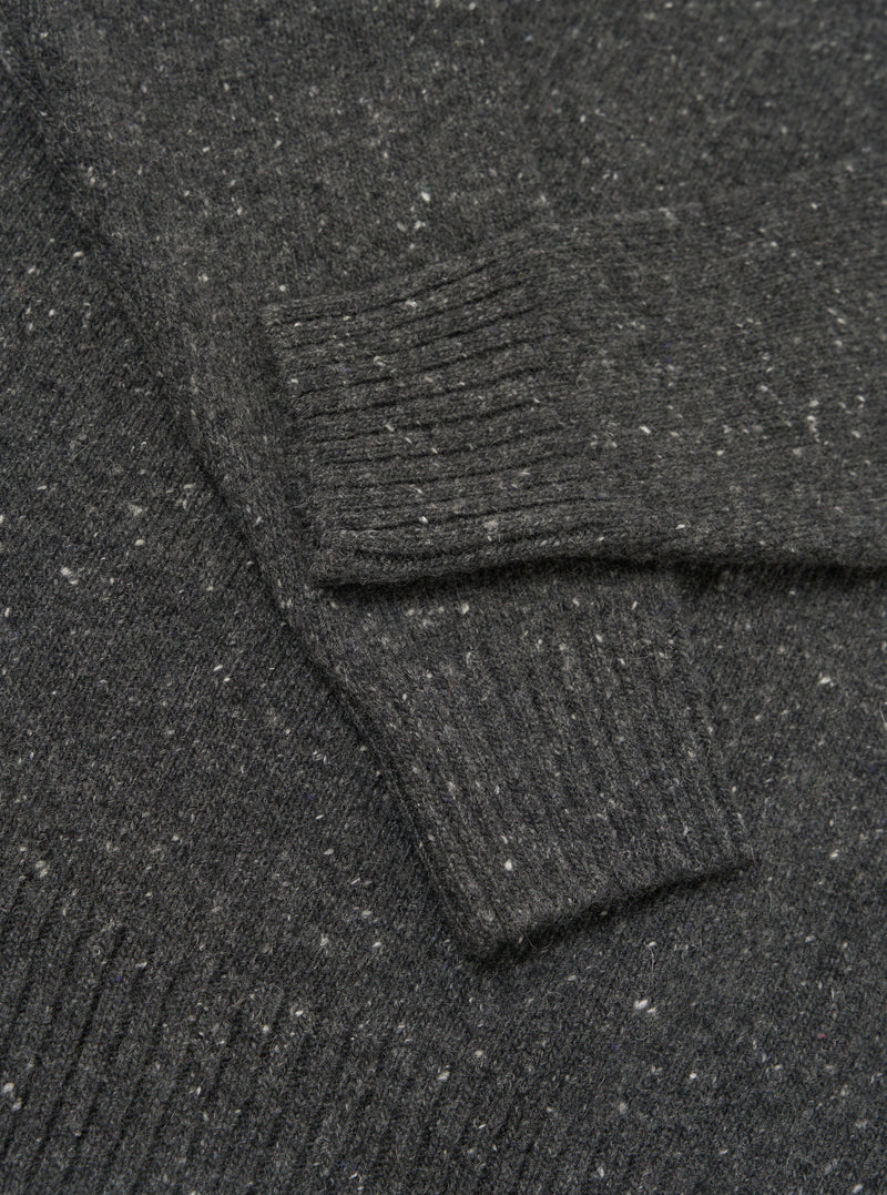 A detailed close-up shot of the Black Wool Fleck Roll Neck, showcasing the fine ribbed collar detail, premium recycled wool fabric, and the distinctive speckled fleck pattern throughout the garment.