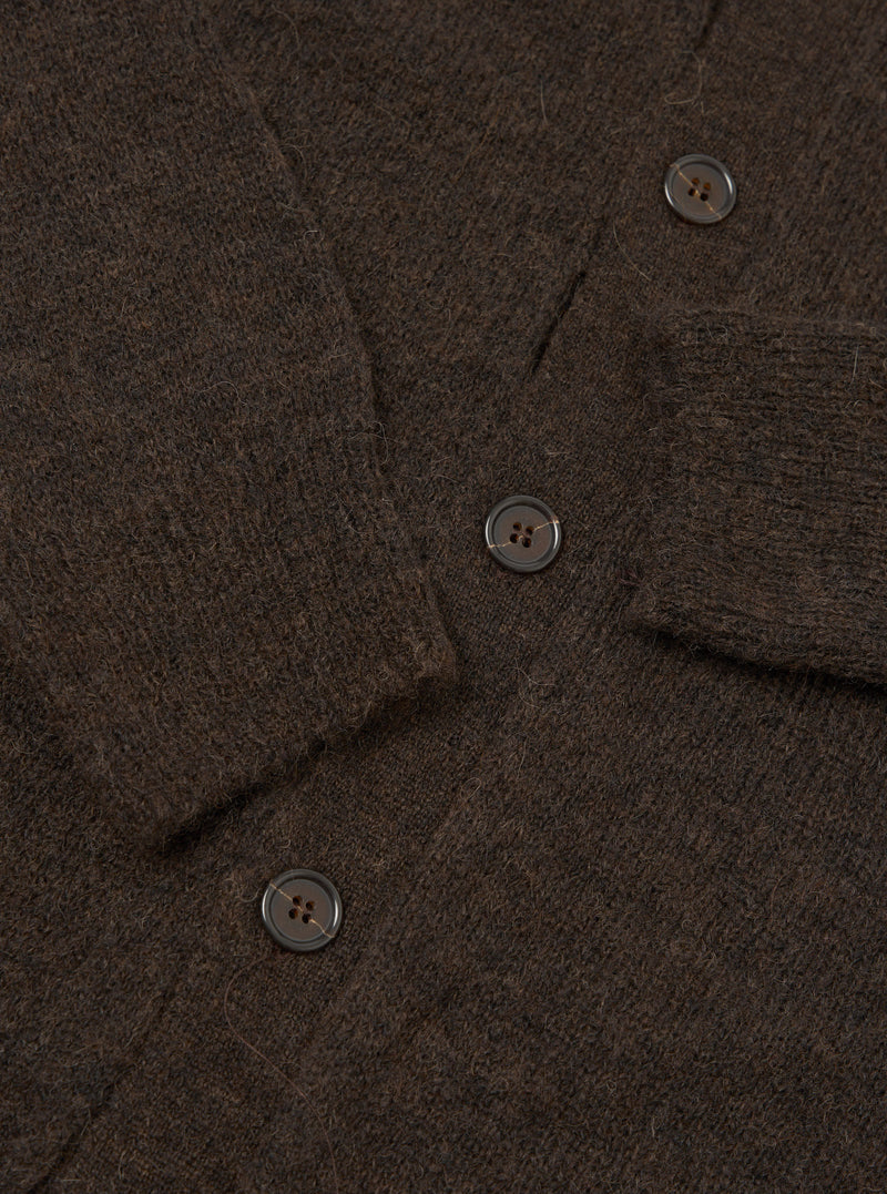 Close-up flat lay of the brown alpaca knit cardigan showing the button placket with three visible dark horn-effect four-hole buttons. The fluffy, hairy texture of the alpaca knit is prominent throughout. A ribbed front band runs along the placket edge, with the sleeve visible in the upper right corner.