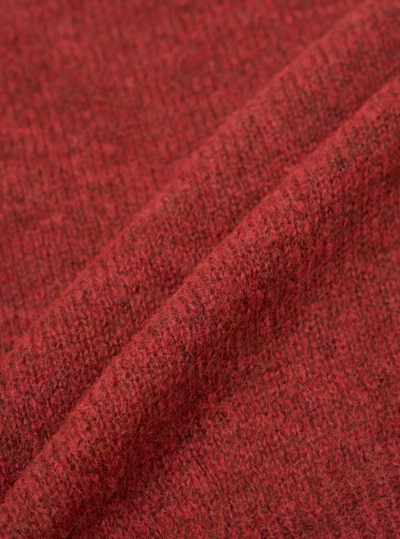 Close-up fabric shot of the deep orange alpaca knit cardigan, showing a folded section of the textile. The marl knit texture is clearly visible, with dark flecks running through the warm red-orange yarn. The soft, slightly hairy surface is characteristic of alpaca fibre. Plain white studio background.