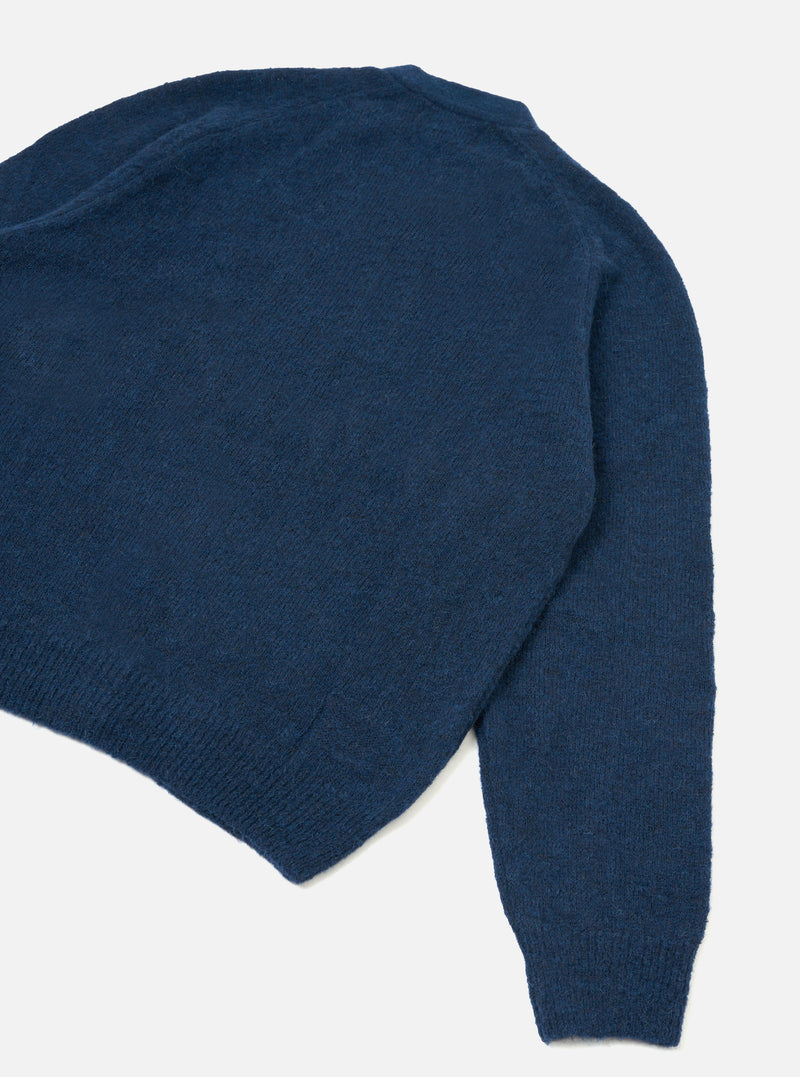 The Navy Alpaca Knit David Cardigan is laid flat on a light grey backdrop, shot from above showing the back body and sleeve. Features a soft, fluffy alpaca knit texture in deep navy blue with ribbed trim along the hem and cuffs.