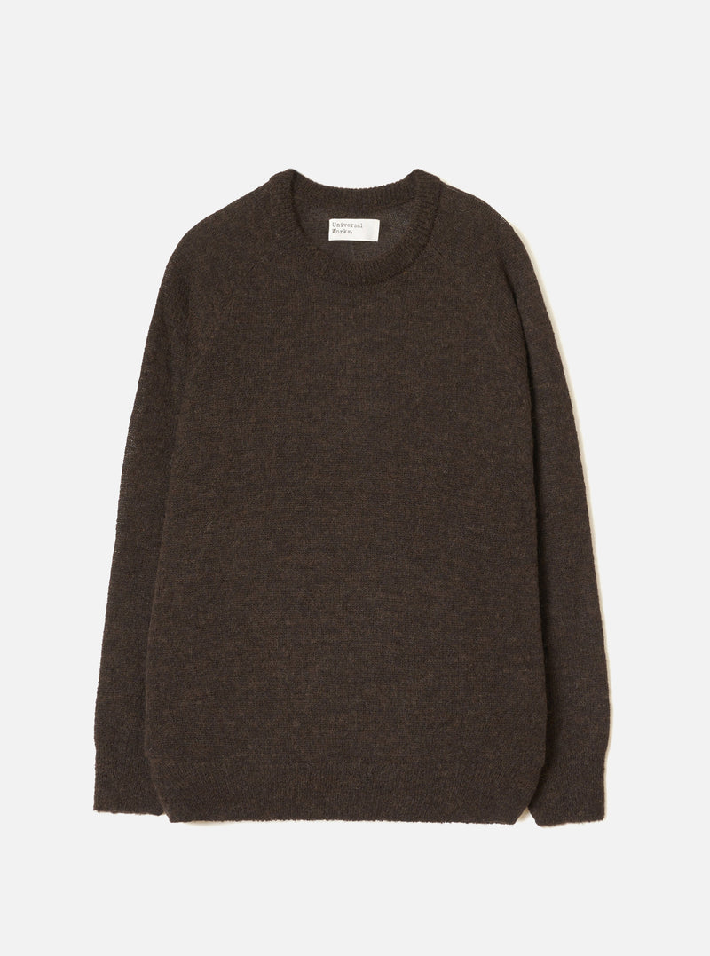 Brown alpaca knit crew neck sweater laid flat on a light grey studio backdrop. Ribbed crew neck collar with a woven Universal Works label at the back. Soft, slightly fluffy alpaca knit texture throughout. Ribbed cuffs and hem. Long sleeves. No fastenings.
