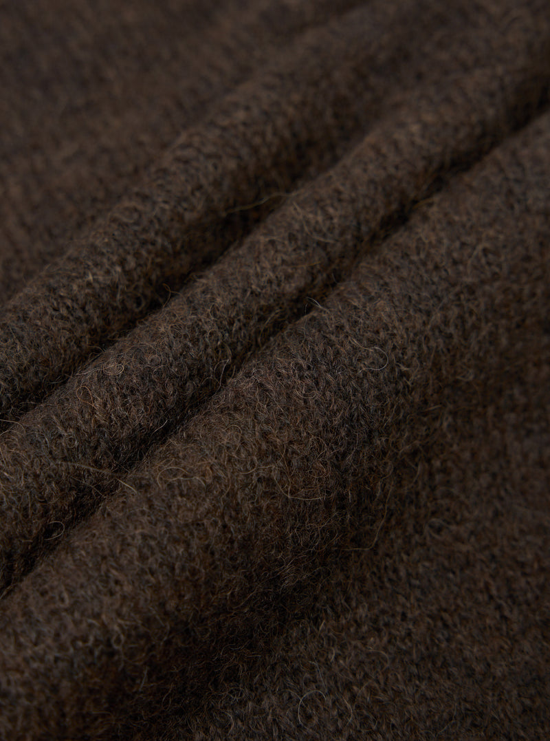 Close-up detail shot of the brown alpaca knit fabric, showing a hairy texture with visible individual fibres. Three soft ridges of folded knit run diagonally across the frame, highlighting the fabric's lofty, textured hand. Dark brown melange colouring throughout.