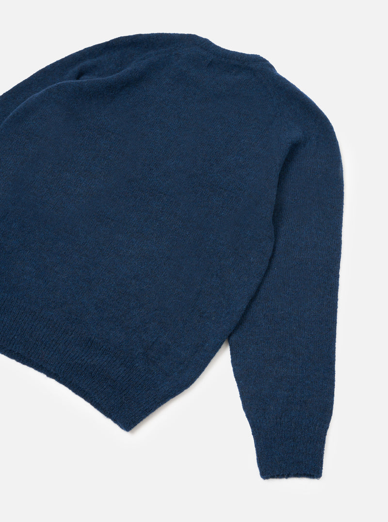 The Navy Alpaca Knit Lyon Crew jumper is laid flat on a light grey backdrop, showing the back and sleeve. Features a soft, slightly fluffy alpaca knit texture in navy blue with a ribbed hem and ribbed sleeve cuffs visible.