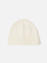 An Ecru Merino Knit Watch Cap displayed flat against a plain studio background. The classic knitted beanie features a soft ribbed texture, a turn-up cuff, and a comfortable stretchy fit in off-white ecru merino wool.