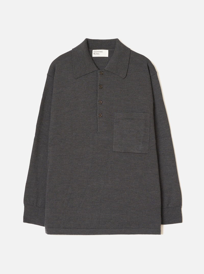 Charcoal merino knit pullover shirt laid flat on a light grey seamless backdrop. Features a wide point collar, four-button placket with dark buttons, a left chest patch pocket, long sleeves with ribbed cuffs, and a ribbed hem. Fine smooth knit texture throughout. Universal Works woven label at back neck.