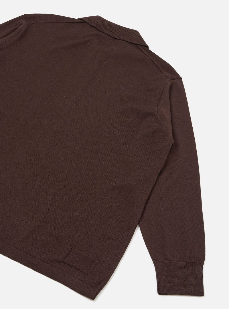 Flat lay detail shot of an espresso brown merino long-sleeve pullover knit shirt on a light grey seamless backdrop. The image shows the upper back, shoulder and one full sleeve. A ribbed polo collar is visible at the top, with a fine knit texture throughout. The cuff is ribbed and the hem has a clean ribbed finish.
