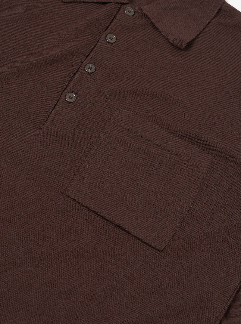 Close-up flat lay of an espresso brown merino knit polo shirt on a plain white surface. The ribbed knit collar, three-button placket with dark four-hole buttons, and a chest patch pocket are clearly visible. The fine knit texture is evident across the body.