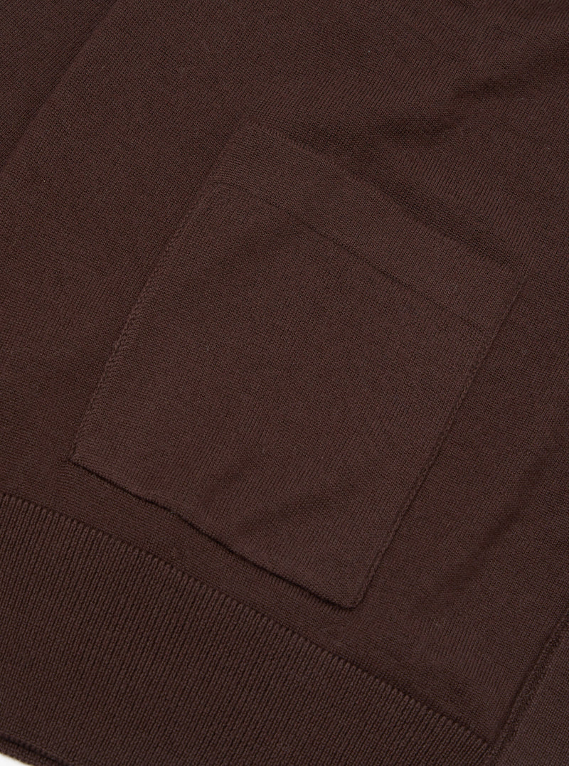Close-up flat lay of the lower section of an espresso brown merino cardigan. A square patch pocket sits above a ribbed hem band. The fine knit texture is visible across the body. Plain white studio backdrop.