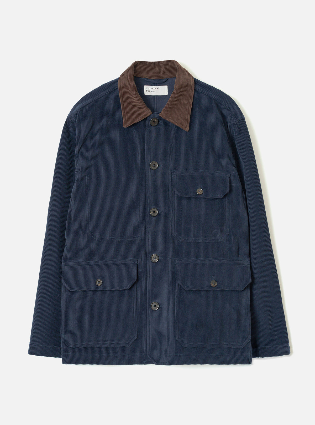 Dark navy corduroy utility jacket laid flat on a light grey studio backdrop. Features a contrast brown corduroy collar, five dark horn buttons at the front placket, two chest patch pockets with button flaps, and two larger patch pockets at the hip with button flaps. Woven brand label visible at the neck.