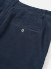 Close-up detail of the rear of dark navy corduroy military chinos, shot flat on a white studio surface. A welt back pocket with a single four-hole button fastening is visible. The wide-wale corduroy texture runs vertically across the fabric. The waistband sits at the top of the frame.