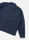 Flat lay of an indigo denim Ives jacket on a light grey backdrop, shot from the rear at an angle. Contrasting white topstitching runs along the shoulder seam, sleeve, and hem. A welt pocket sits at the hip and rectangular bartack details appear at the chest yoke and hem. The cuff and straight hem are visible.