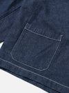 Close-up flat lay of the indigo future denim Ives jacket on a white surface, showing a large patch pocket with contrast white topstitching and angled bartack reinforcement at the corners. The hem and pocket base feature the same white stitching. The slubby denim texture is visible throughout.