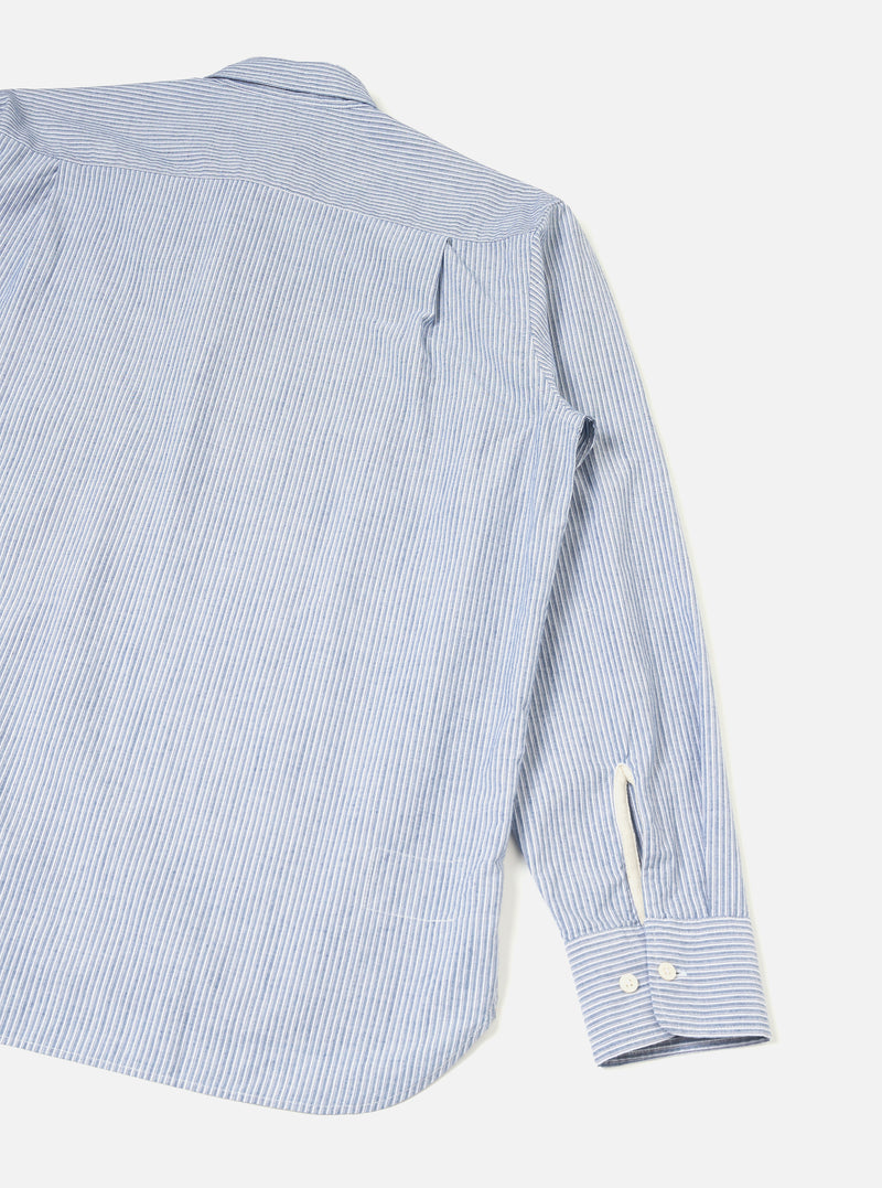 Rear view of the Blue Montgomery Stripe Station Shirt displayed on a clean neutral background. The photograph showcases the vertical blue striped cotton fabric, straight hemline, neat shoulder yoke, and back pleat construction of the garment.