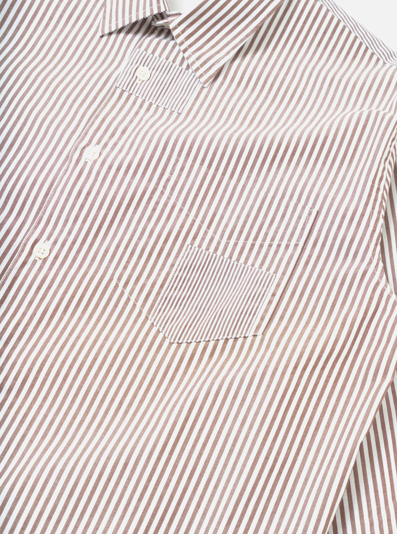Close-up flat lay of a brown and white striped cotton shirt on a white background. The point collar, button placket with white buttons, and a chest patch pocket are visible. The pocket features a contrasting finer stripe panel. Topstitching outlines the pocket and placket seams.