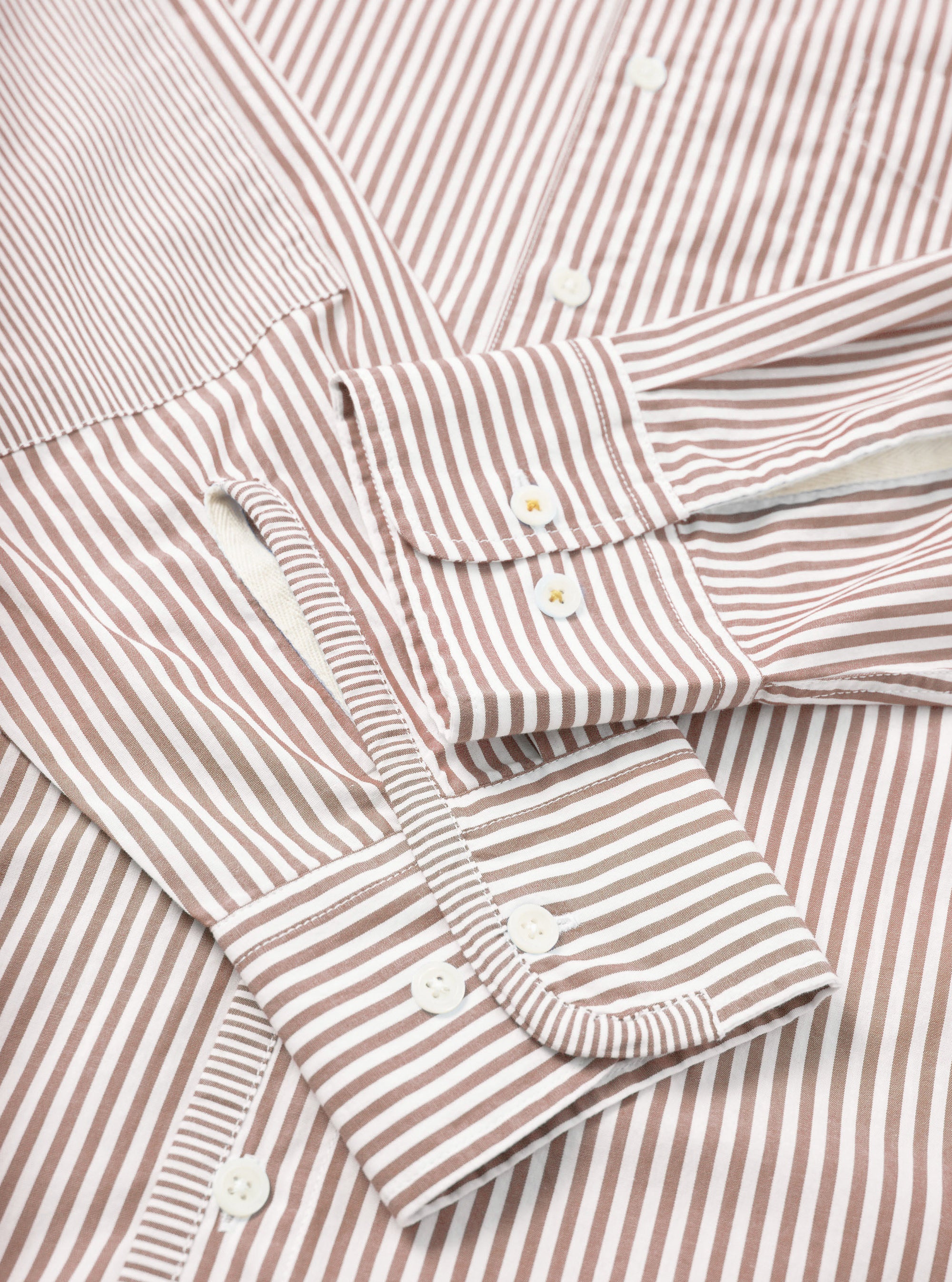 Close-up flat lay of the brown and white striped Queens Cotton Patched Shirt. The shot focuses on the cuffs and front placket. Both barrel cuffs feature white buttons, with additional buttons visible on the placket. Fine Bengal stripes run across a smooth cotton fabric.