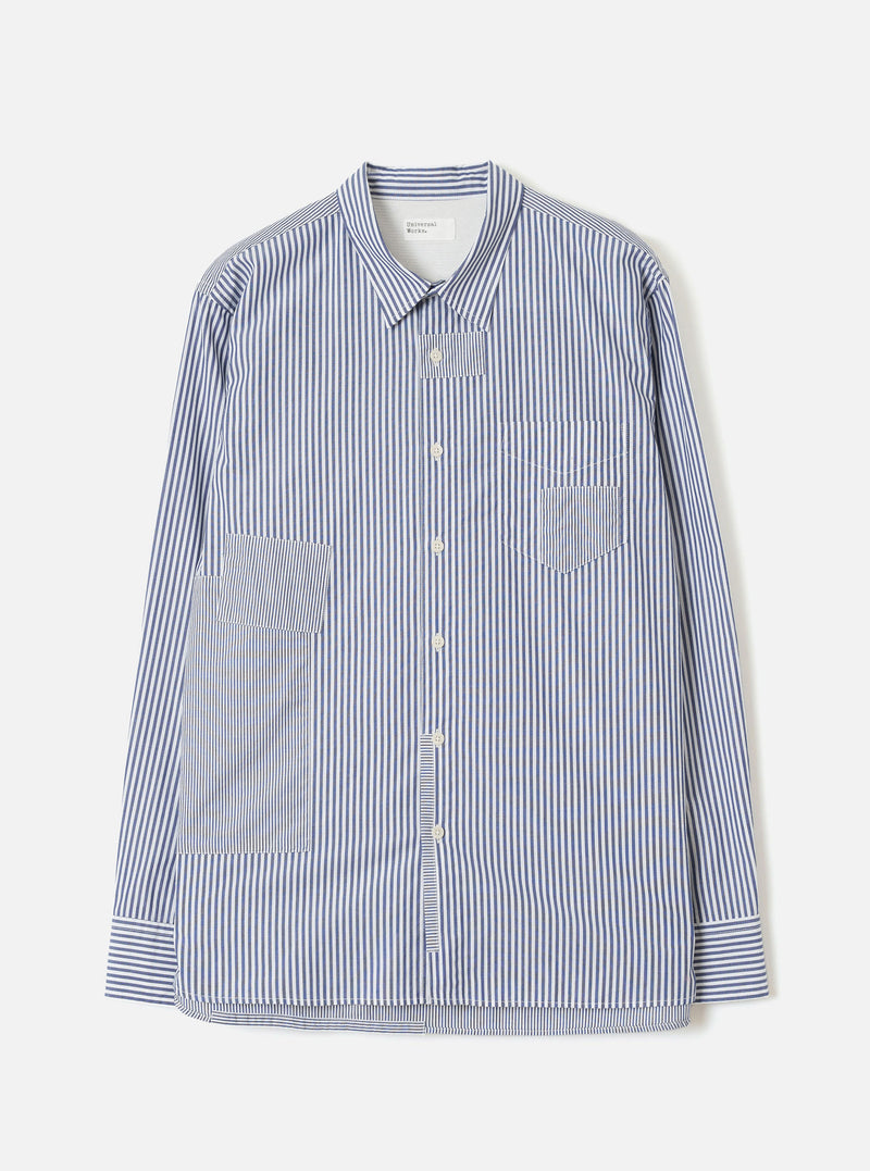 Navy and white vertical-stripe cotton shirt, flat lay on a light grey seamless backdrop. Spread collar, button-through placket with cream buttons, one chest patch pocket and two large front patch pockets. Long sleeves with buttoned cuffs. Topstitched hem with a curved silhouette. Universal Works label visible at the collar.