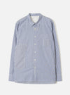 Navy and white vertical-stripe cotton shirt, flat lay on a light grey seamless backdrop. Spread collar, button-through placket with cream buttons, one chest patch pocket and two large front patch pockets. Long sleeves with buttoned cuffs. Topstitched hem with a curved silhouette. Universal Works label visible at the collar.
