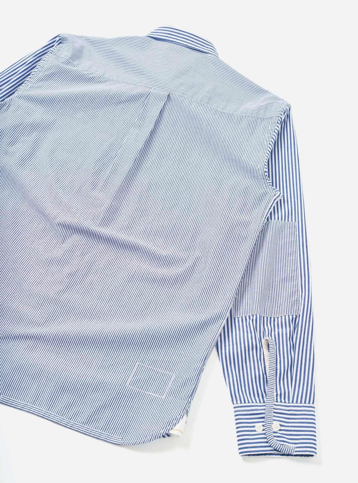 Navy and white fine-stripe cotton shirt laid flat on a white surface, shot from above at an angle. The back yoke and a centre pleat are visible. One sleeve extends to a buttoned barrel cuff with two white buttons. A small chest patch pocket is visible on the sleeve.