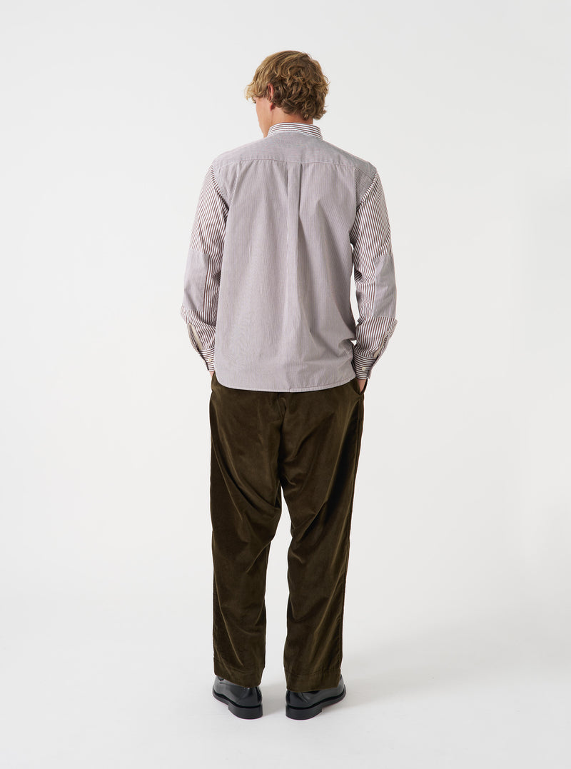 A male model wears the Brown Queens Cotton Patched Shirt posed against a plain studio background. This shot showcases the relaxed fit, woven stripe texture, and distinct patched design from a side angle.