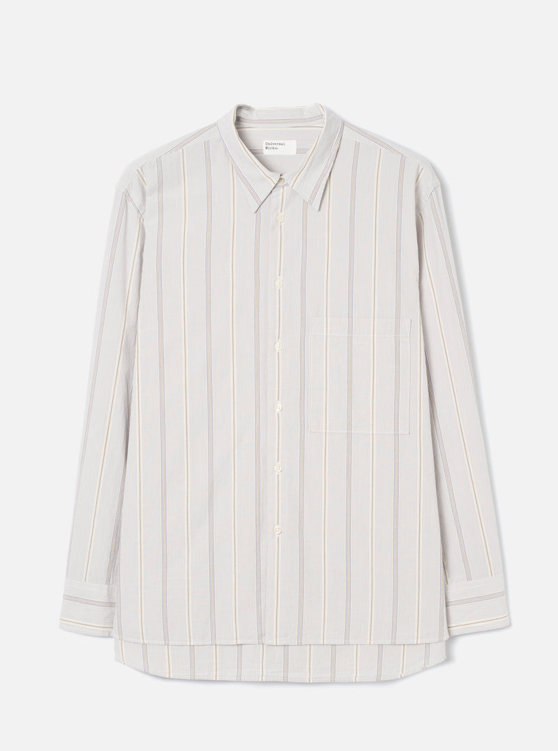 Dove grey long-sleeve shirt in an organic woven stripe, with blue and tan vertical stripes on a light ground. Point collar, concealed button placket with five buttons, one square chest patch pocket, and buttoned cuffs. Universal Works woven label at neck. Flat lay on a light grey seamless backdrop.