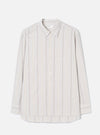 Dove grey long-sleeve shirt in an organic woven stripe, with blue and tan vertical stripes on a light ground. Point collar, concealed button placket with five buttons, one square chest patch pocket, and buttoned cuffs. Universal Works woven label at neck. Flat lay on a light grey seamless backdrop.