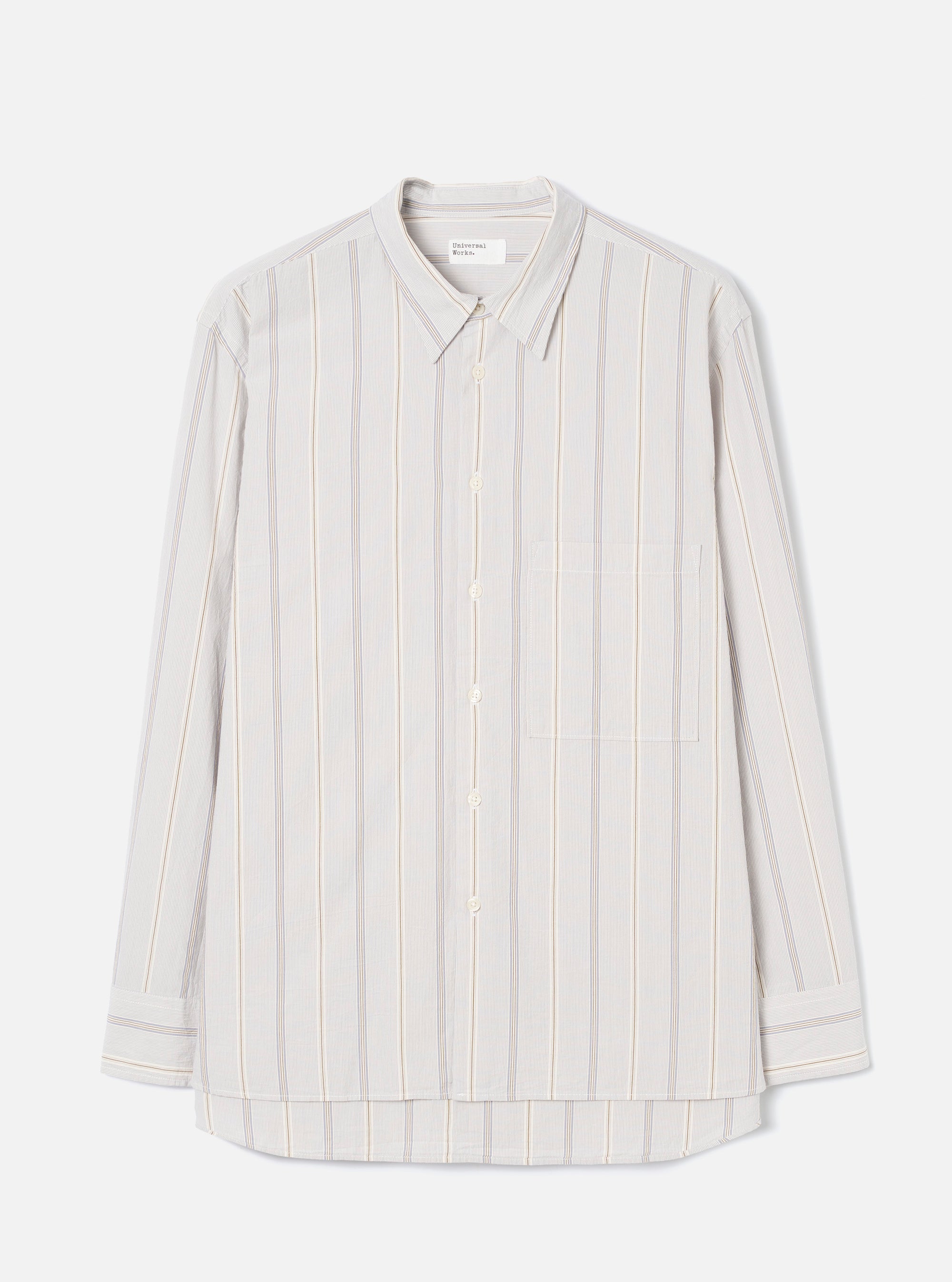 Dove grey long-sleeve shirt in an organic woven stripe, with blue and tan vertical stripes on a light ground. Point collar, concealed button placket with five buttons, one square chest patch pocket, and buttoned cuffs. Universal Works woven label at neck. Flat lay on a light grey seamless backdrop.