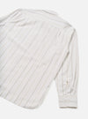 Flat lay of the Dove Monk Organic Stripe Square Pocket Shirt on a white studio backdrop, shot from above at an angle showing the back and one sleeve. Off-white woven fabric with vertical tan and grey pinstripes. Spread collar and buttoned cuff visible, with a curved hem at the base.