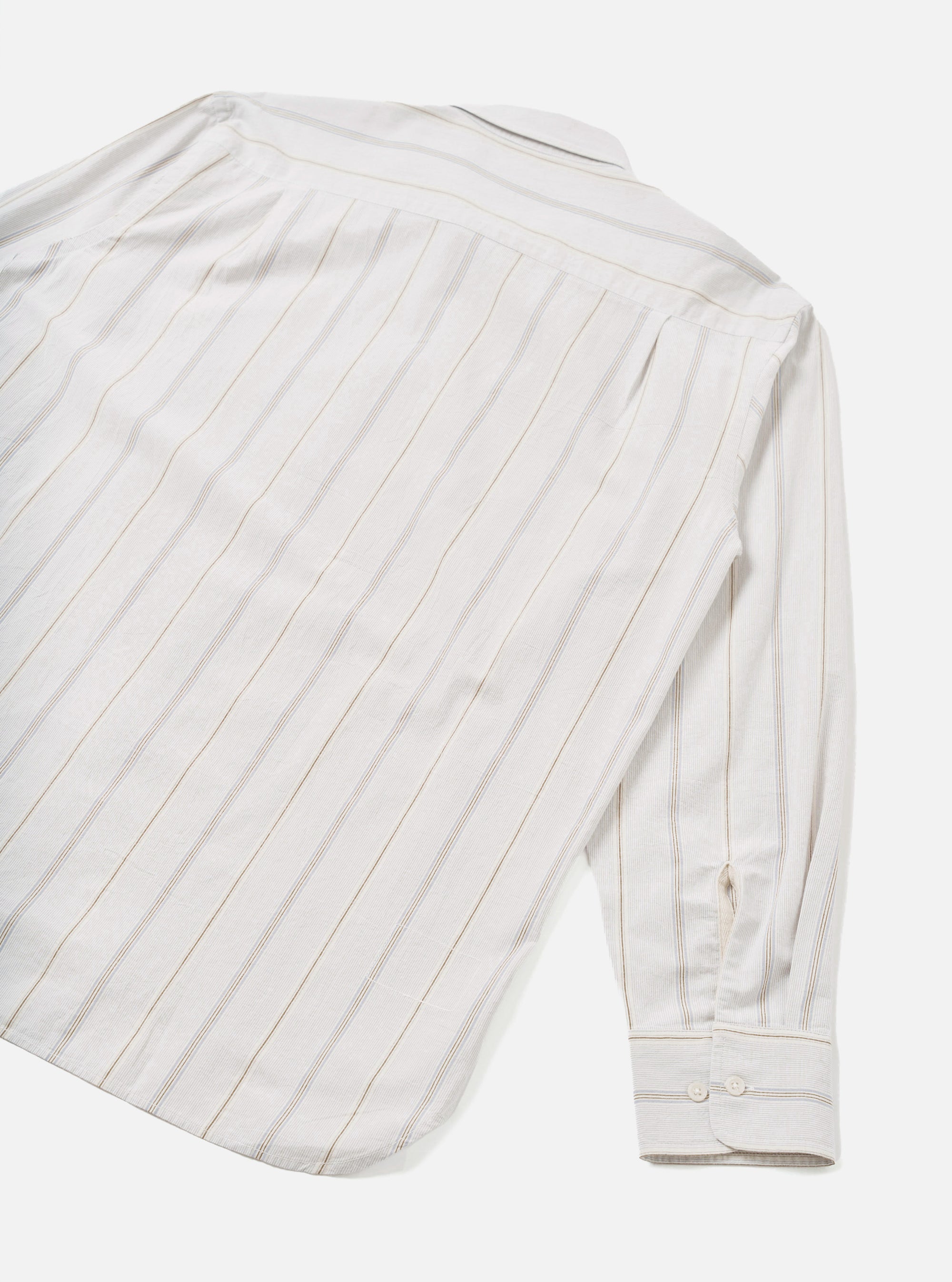 Flat lay of the Dove Monk Organic Stripe Square Pocket Shirt on a white studio backdrop, shot from above at an angle showing the back and one sleeve. Off-white woven fabric with vertical tan and grey pinstripes. Spread collar and buttoned cuff visible, with a curved hem at the base.