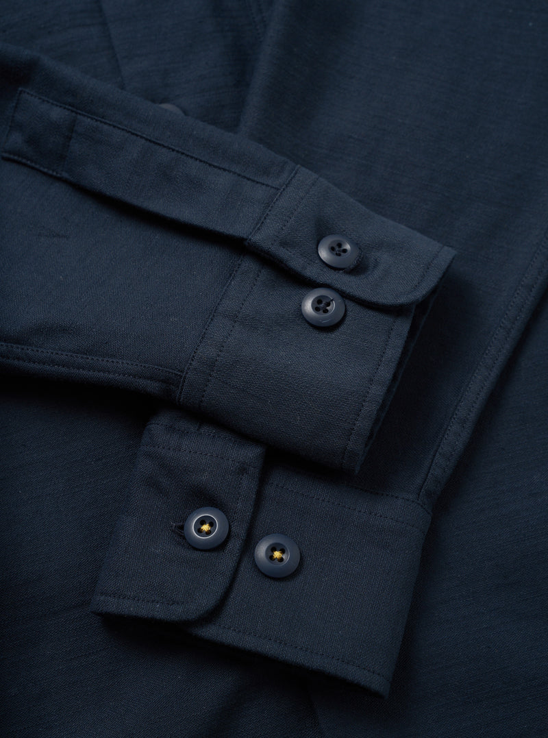 A side profile view of the Navy Slub Sateen Fatigue Shirt displayed against a white studio background. The image highlights the sleeve cuff details, side seam tailoring, and textured cotton fabric.