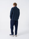 A male model wearing the Navy Slub Sateen Fatigue Shirt is captured from the back against a plain white background. The shot displays the relaxed shoulder fit and casual length of the garment.