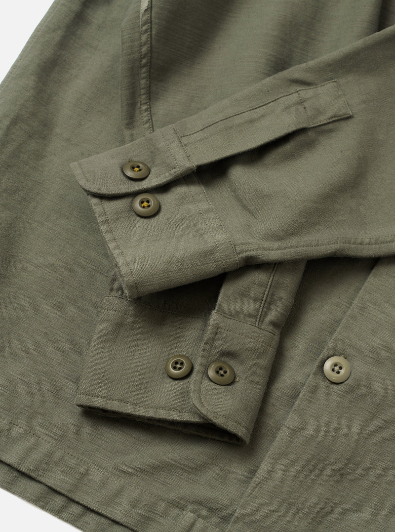 A side profile shot of the Olive Slub Sateen Fatigue Shirt displayed against a simple white backdrop. The view highlights the sleeve construction, cuff details, and relaxed fit of the olive overshirt.