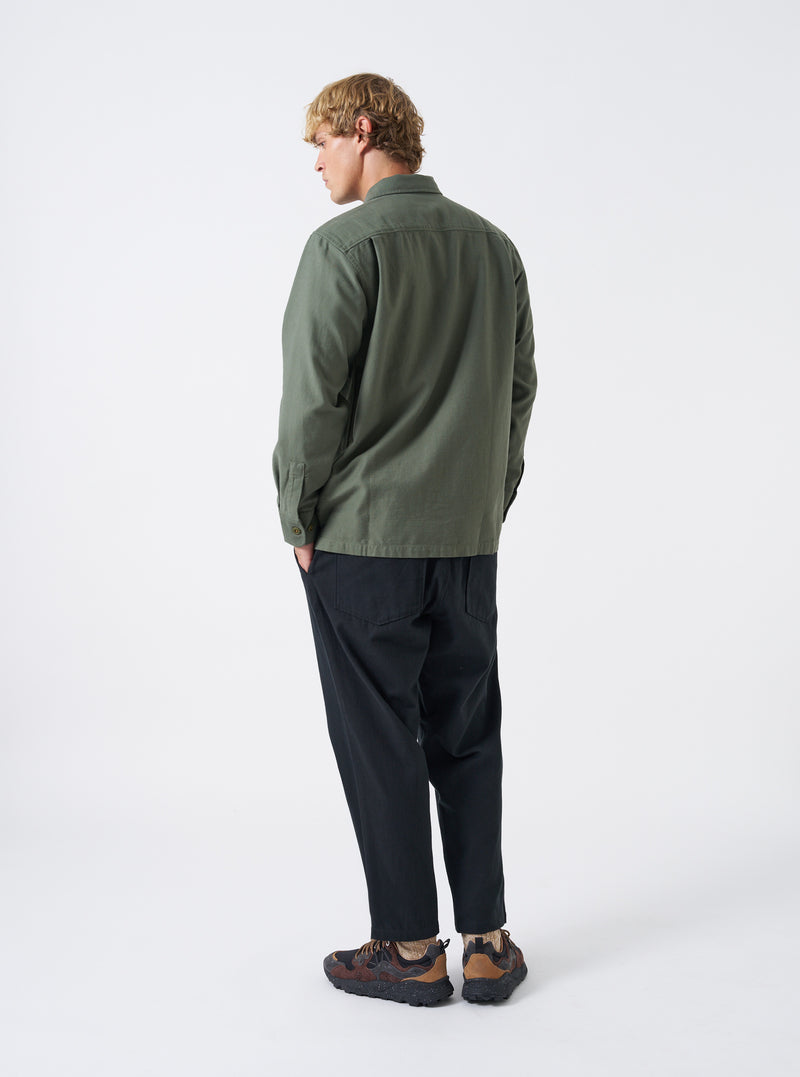 A male model is pictured from the back wearing the Olive Slub Sateen Fatigue Shirt against a plain white backdrop. The shot details the comfortable fit across the shoulders and the clean rear hem.