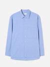 Flat lay of a blue brushed flannel shirt on a light grey studio backdrop. Features a pointed collar, full-length sleeves with plain cuffs, a buttoned placket with six small white buttons, and a square patch pocket on the left chest. The curved shirttail hem is visible at the front. Fabric has a soft, lightly textured finish.