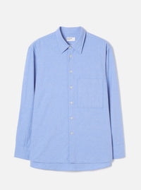 Flat lay of a blue brushed flannel shirt on a light grey studio backdrop. Features a pointed collar, full-length sleeves with plain cuffs, a buttoned placket with six small white buttons, and a square patch pocket on the left chest. The curved shirttail hem is visible at the front. Fabric has a soft, lightly textured finish.