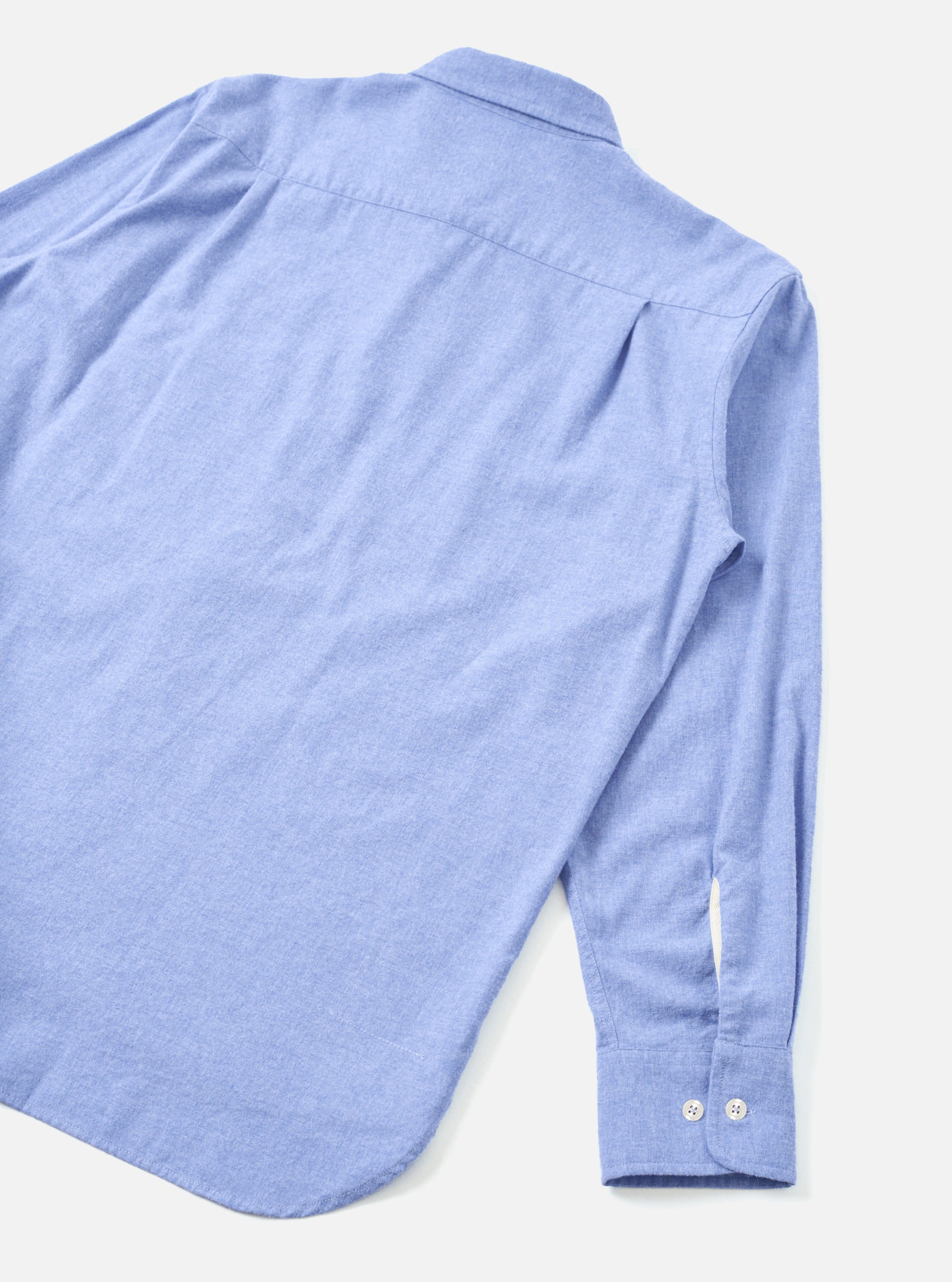 Flat lay of the back of a blue brushed flannel shirt on a light grey seamless backdrop. The woven fabric has a soft, mélange texture. Visible details include a back yoke seam, a spread collar at the top, and a long sleeve with a buttoned cuff fastened with two small white buttons.