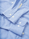Close-up flat lay of a blue brushed flannel shirt showing both cuffs. Each rounded cuff fastens with two white buttons. The soft, lightly mottled flannel texture is visible across the fabric. A white care label is visible at the top. Shot on a plain white studio backdrop.